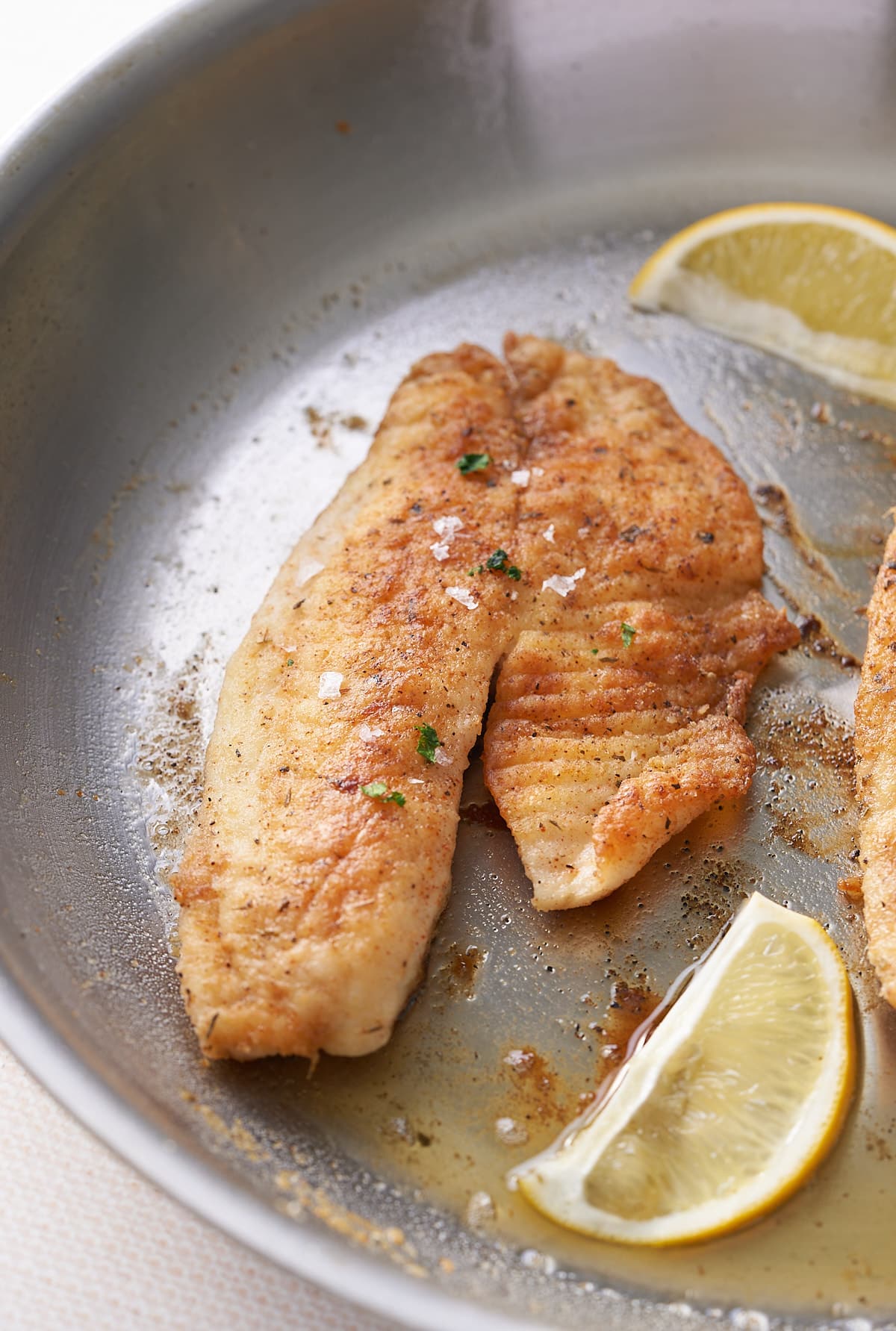Pan fried fish in a large skillet with added slices of fresh lemon.