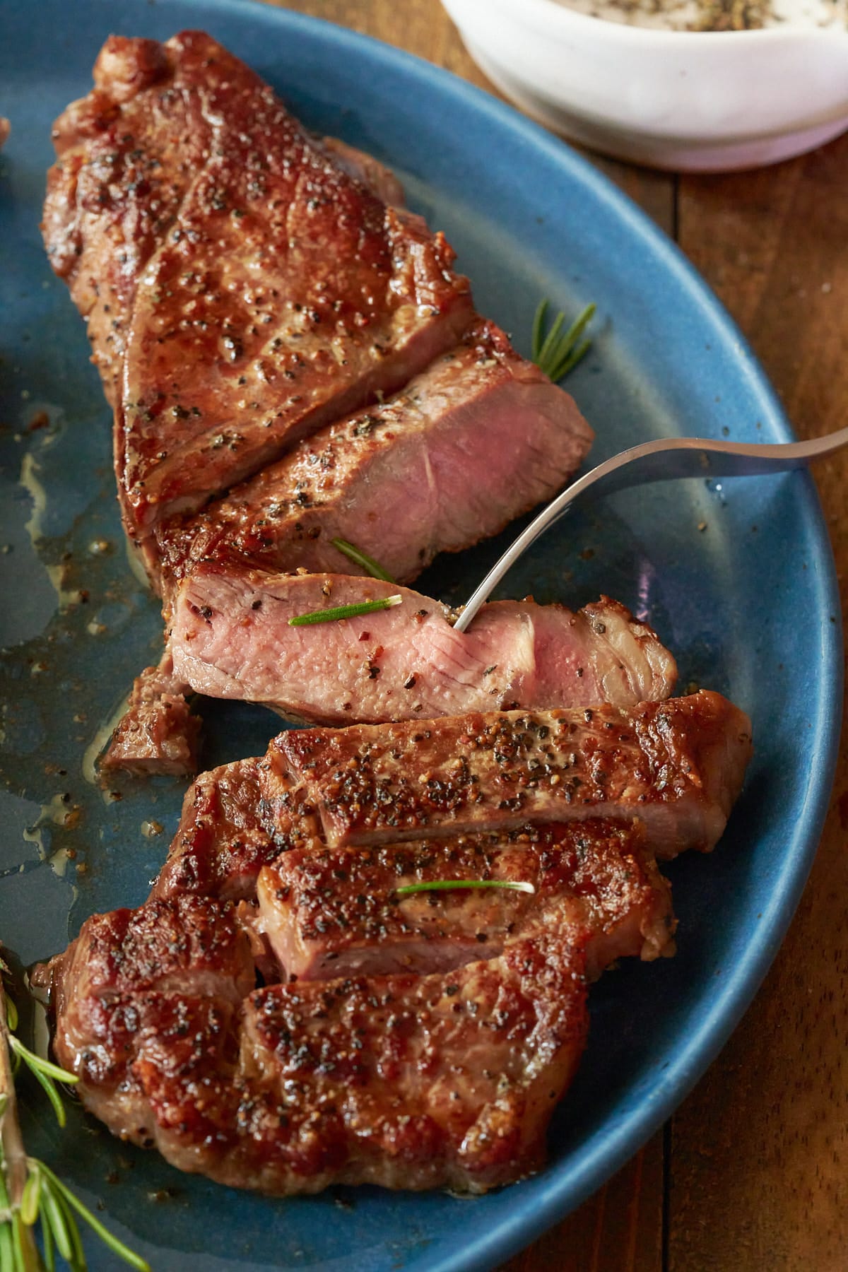 sliced pan seared steak on blue plate with fork picking up a piece