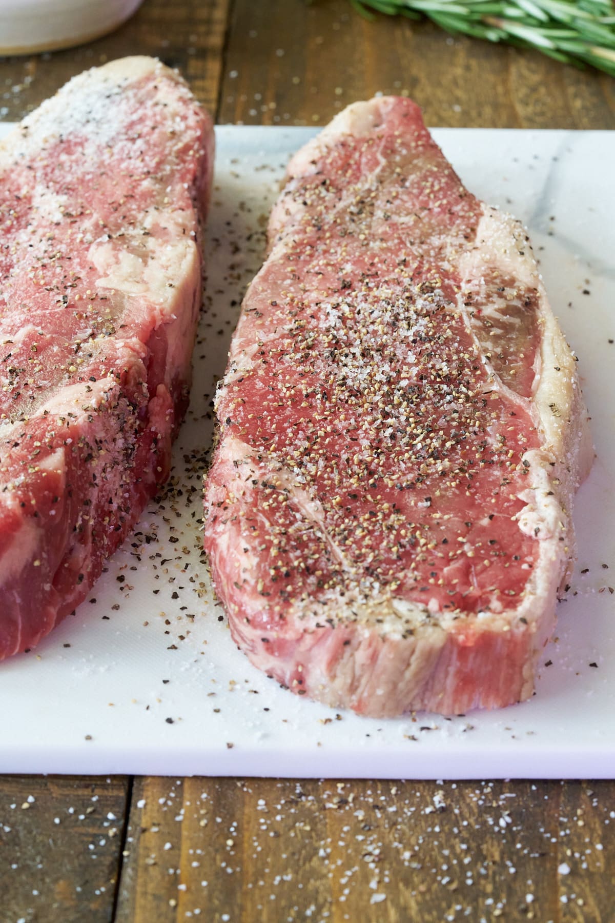 Two seasoned sirloin steaks on a cutting board.
