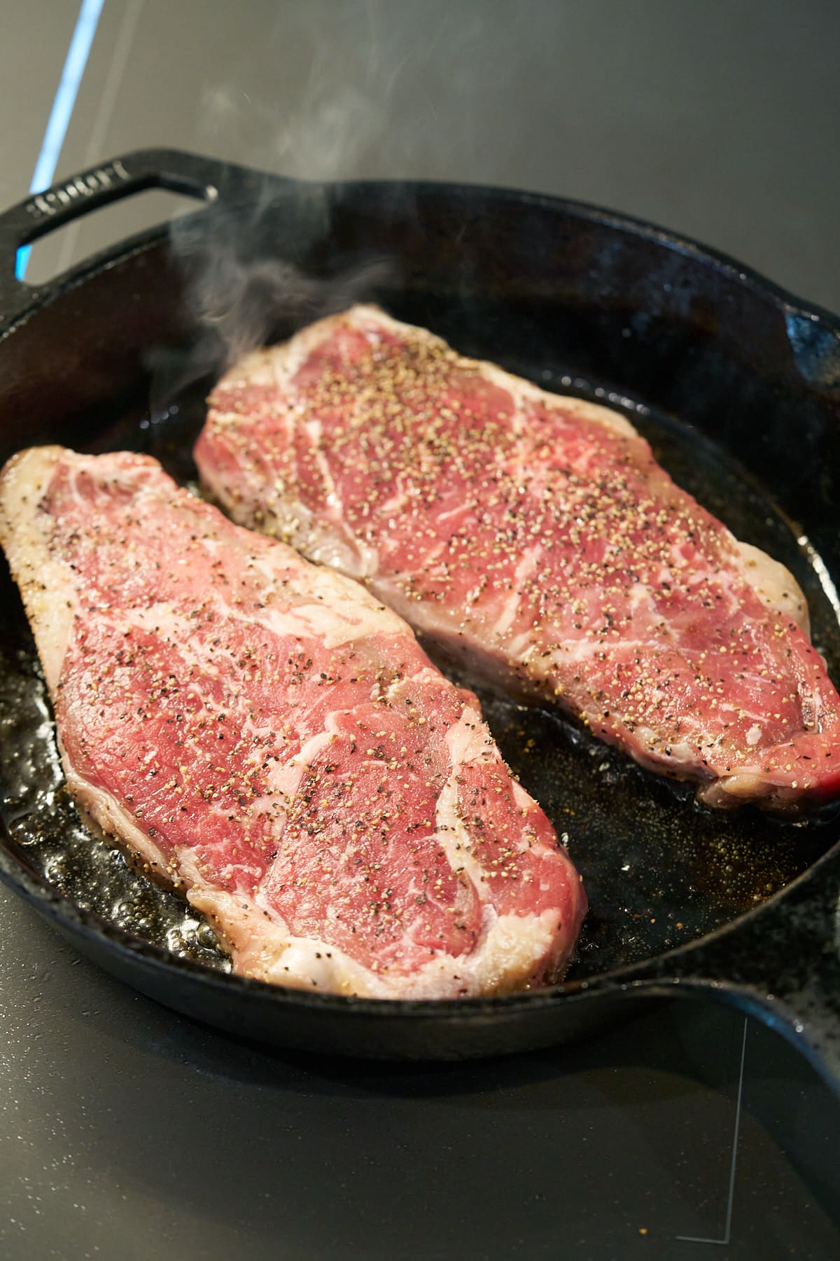 Two seasoned sirloin steaks searing in a cast iron skillet.