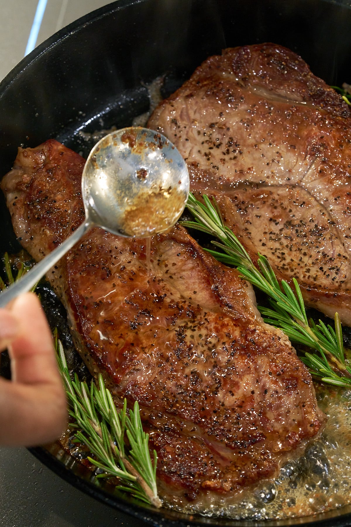 Two seared sirloin steaks in a cast iron skillet with melted butter and pan juices being spooned over the top.