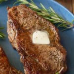 A pan seared sirloin steak, topped with a knob of butter and served on a plate.