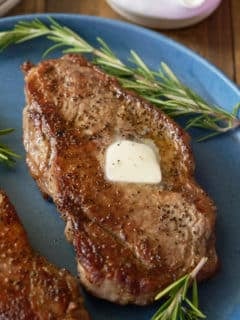 A pan seared sirloin steak, topped with a knob of butter and served on a plate.