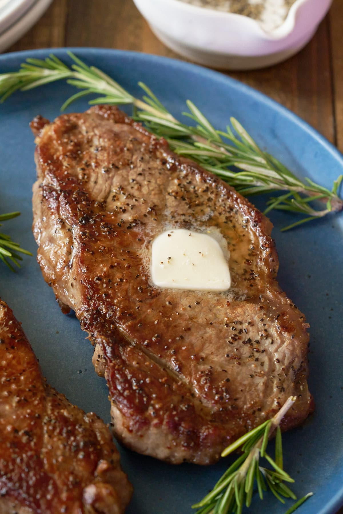 A pan seared sirloin steak, topped with a knob of butter and served on a plate.