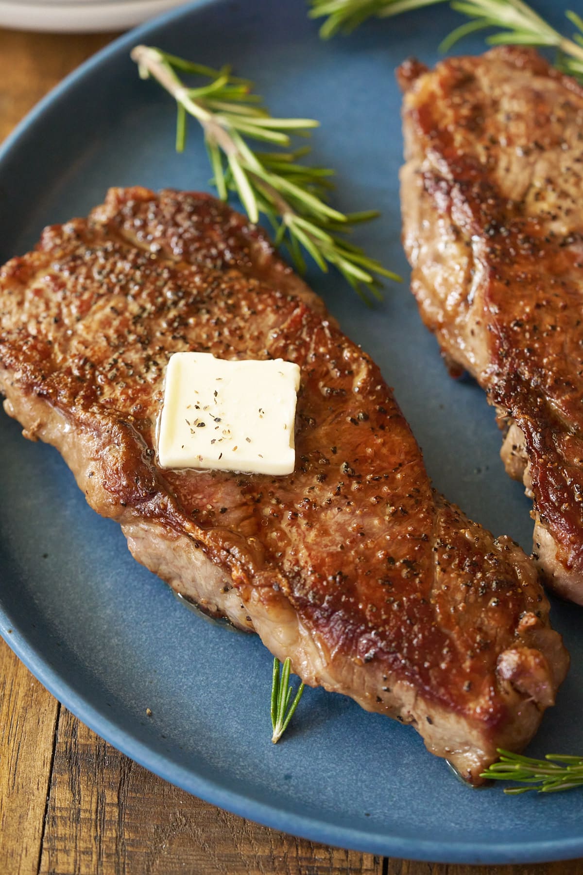 A pan seared sirloin steak, topped with a knob of butter and served on a plate.