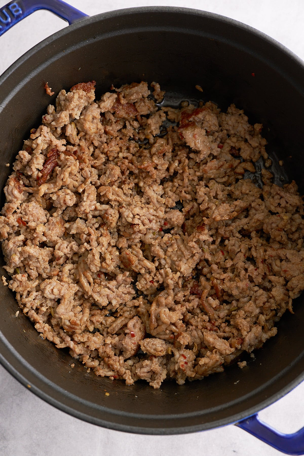 A Dutch oven filled with sauteed Italian sausage.