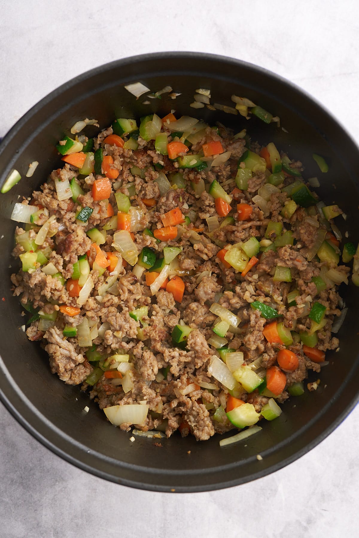 A Dutch oven filled with cooked Italian sausage and sauteed vegetables.