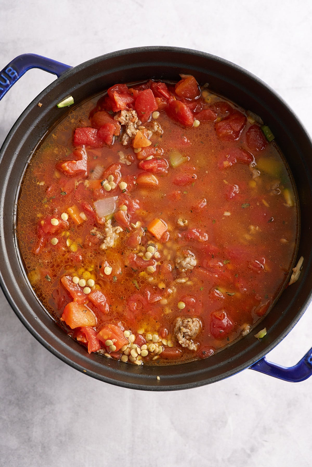 A Dutch oven filled with sausage lentil soup ingredients.