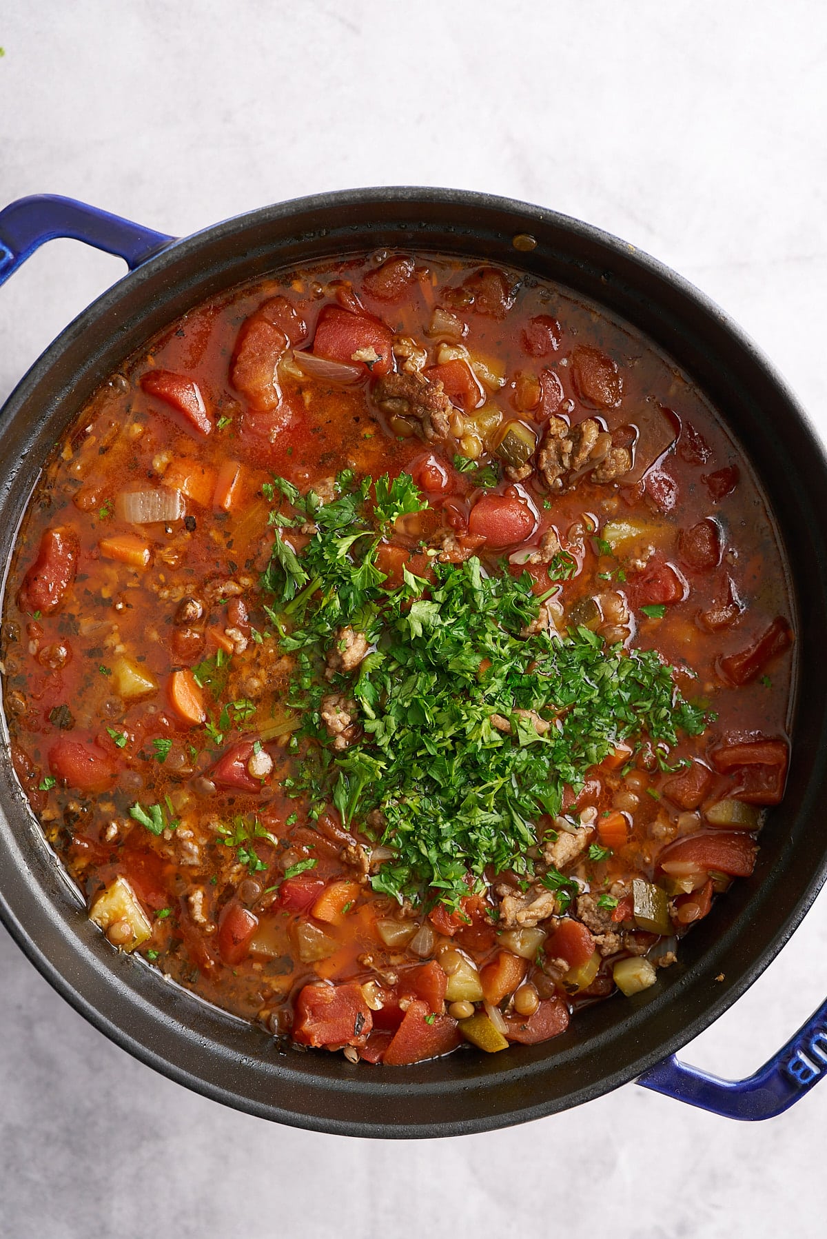 A Dutch oven filled with cooked sausage lentil soup with added fresh parsley.