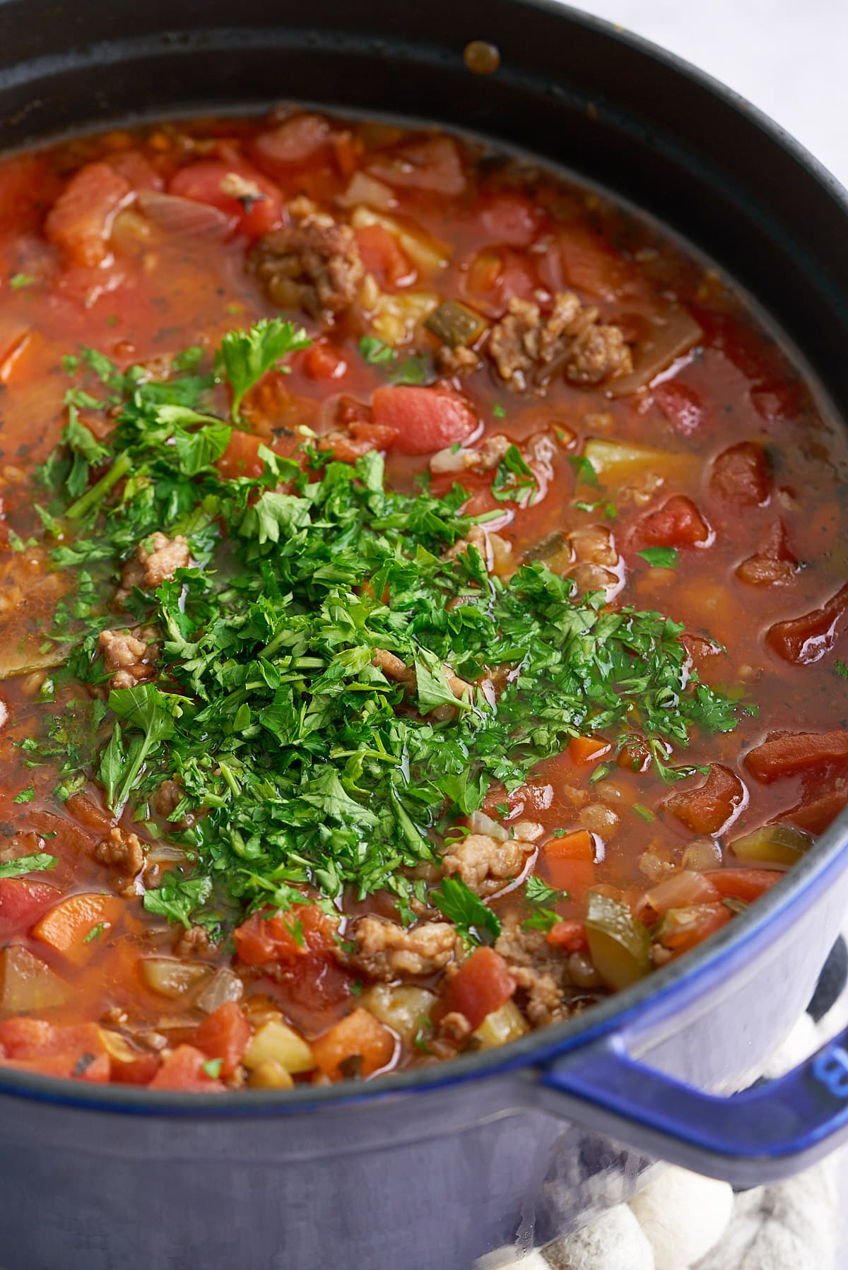 A Dutch oven filled with cooked sausage lentil soup with added fresh parsley.