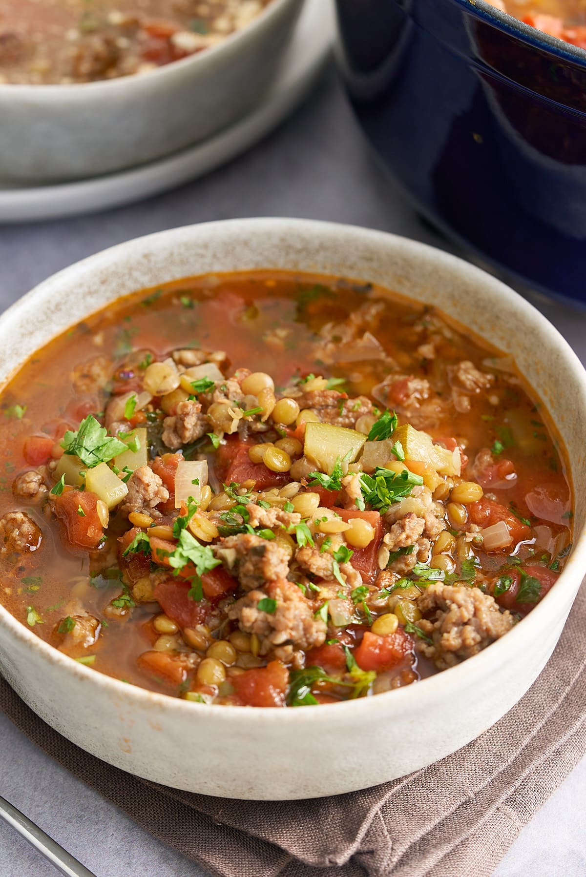 A bowl of sausage lentil soup garnished with some freshly chopped parsley.