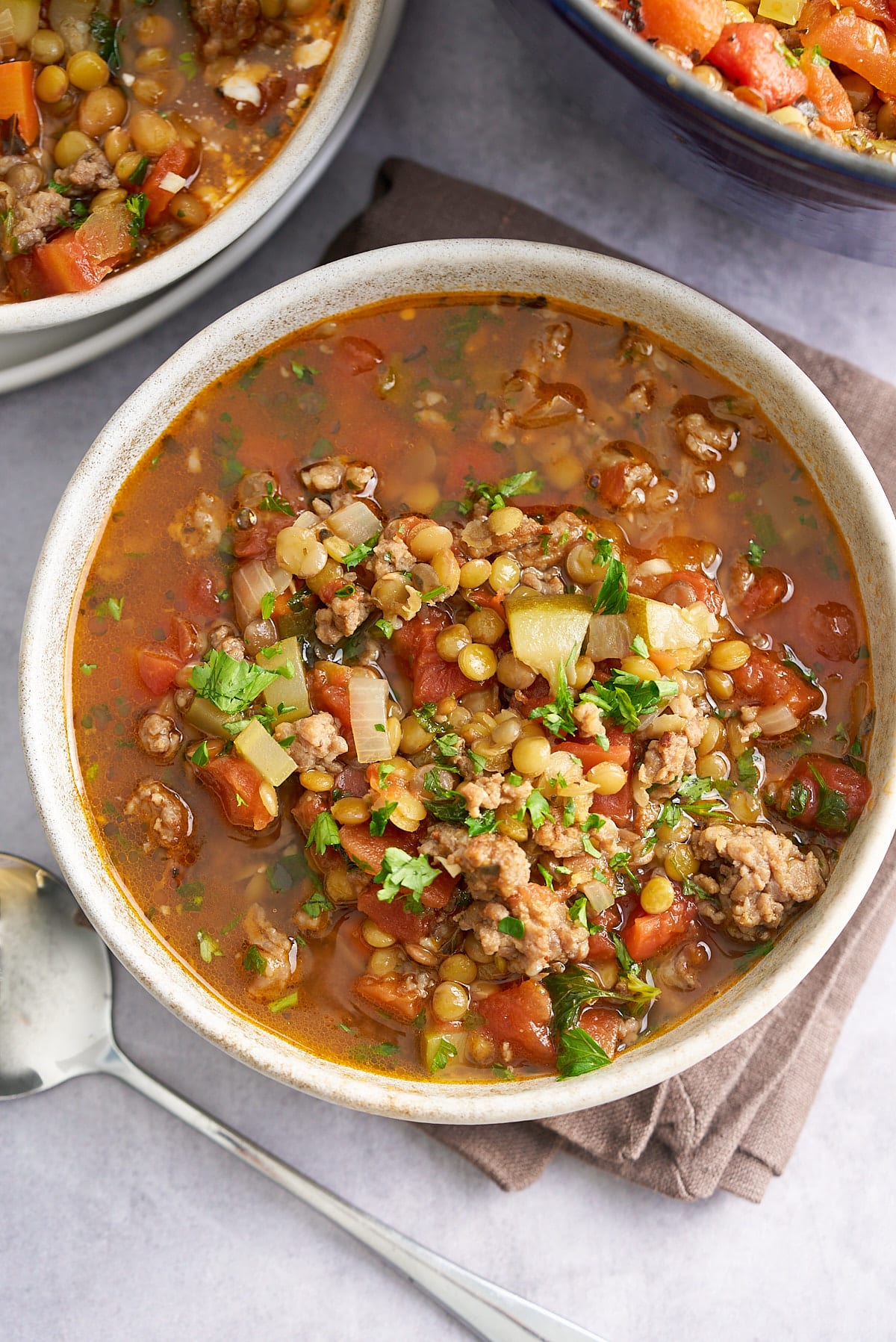 A bowl of sausage lentil soup garnished with some freshly chopped parsley.