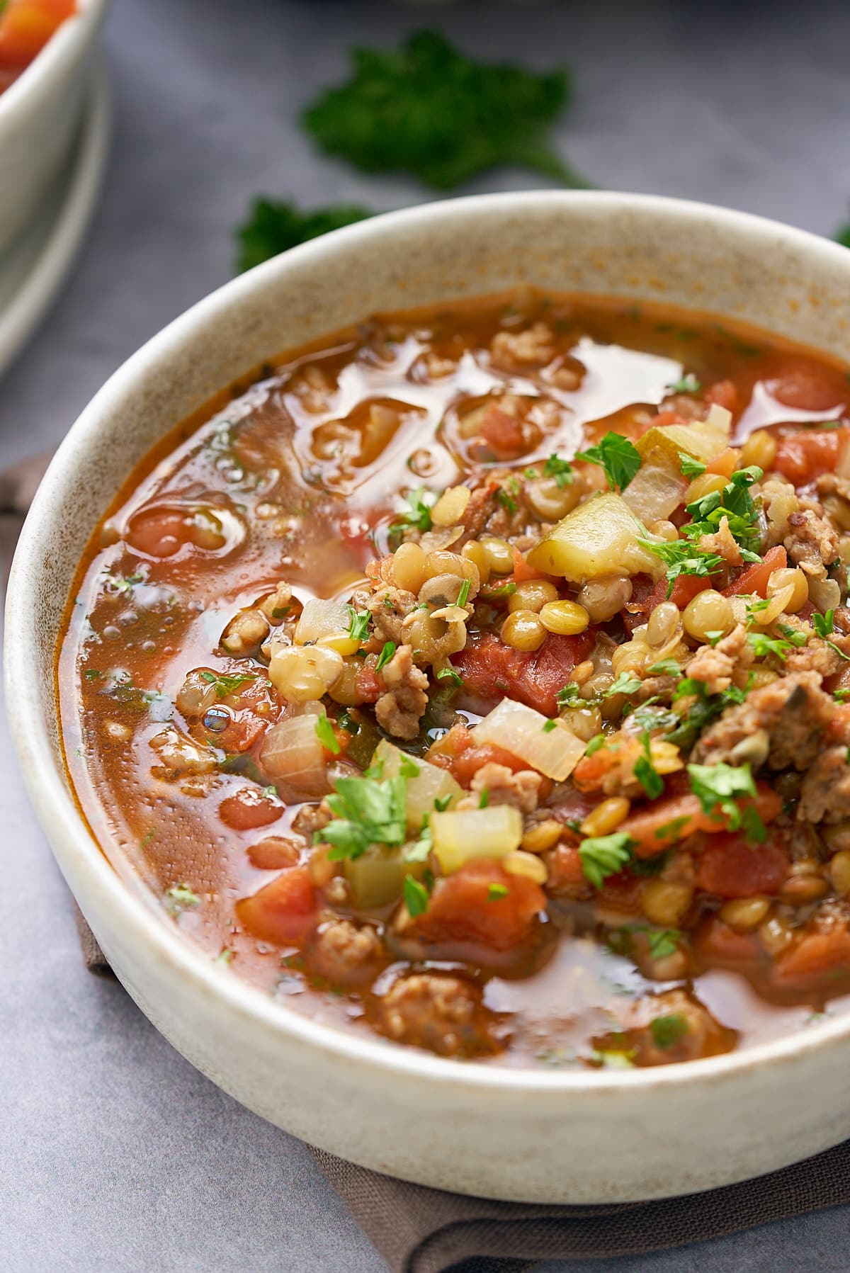 A bowl of sausage lentil soup garnished with some freshly chopped parsley.