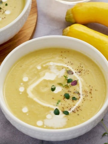yellow squash soup in bowl with yellow squash in back