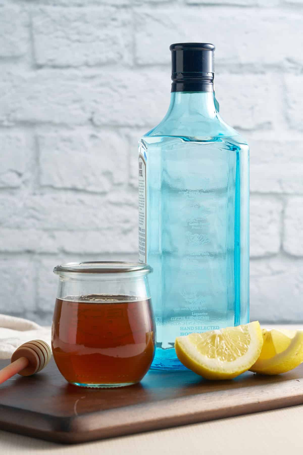 ingredients for the bees knees cocktail. slices of lemon, honey syrup, and bottle of gin