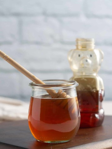 honey simple syrup in glass container in front of a honey bear container