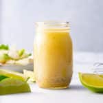 lime vinaigrette in glass bottle with limes and salad around it
