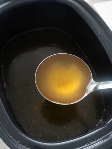 spoon picking up broth from the slow cooker