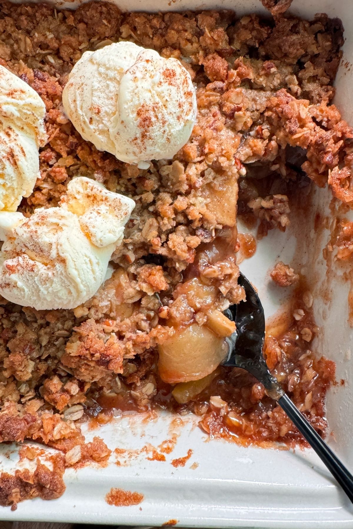 apple crisp with spoon spooning out some and ice cream on top