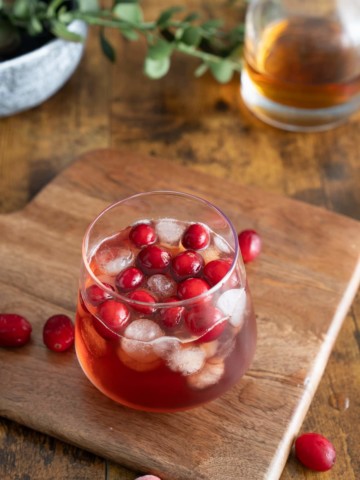 whiskey cranberry cocktail on board with cranberies around it