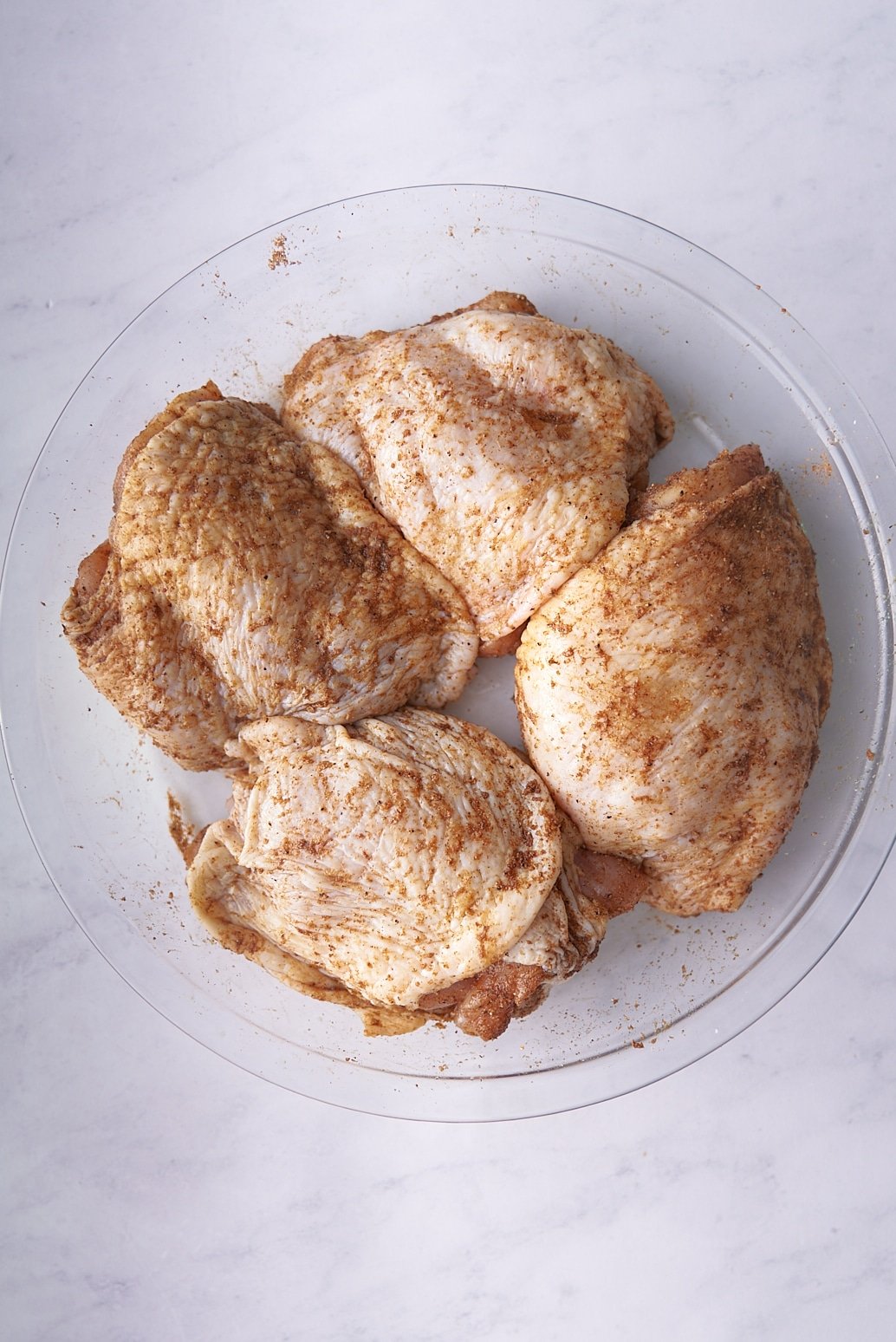 seasoned raw chicken thighs on glass plate