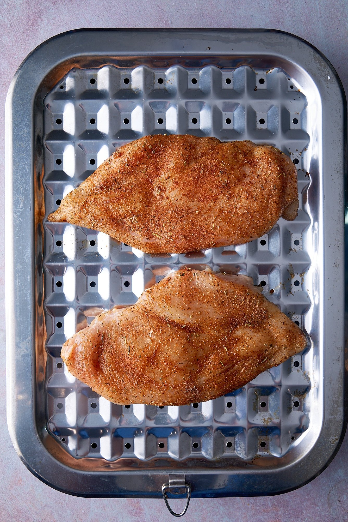 raw seasoned chicken breast on broiler plate