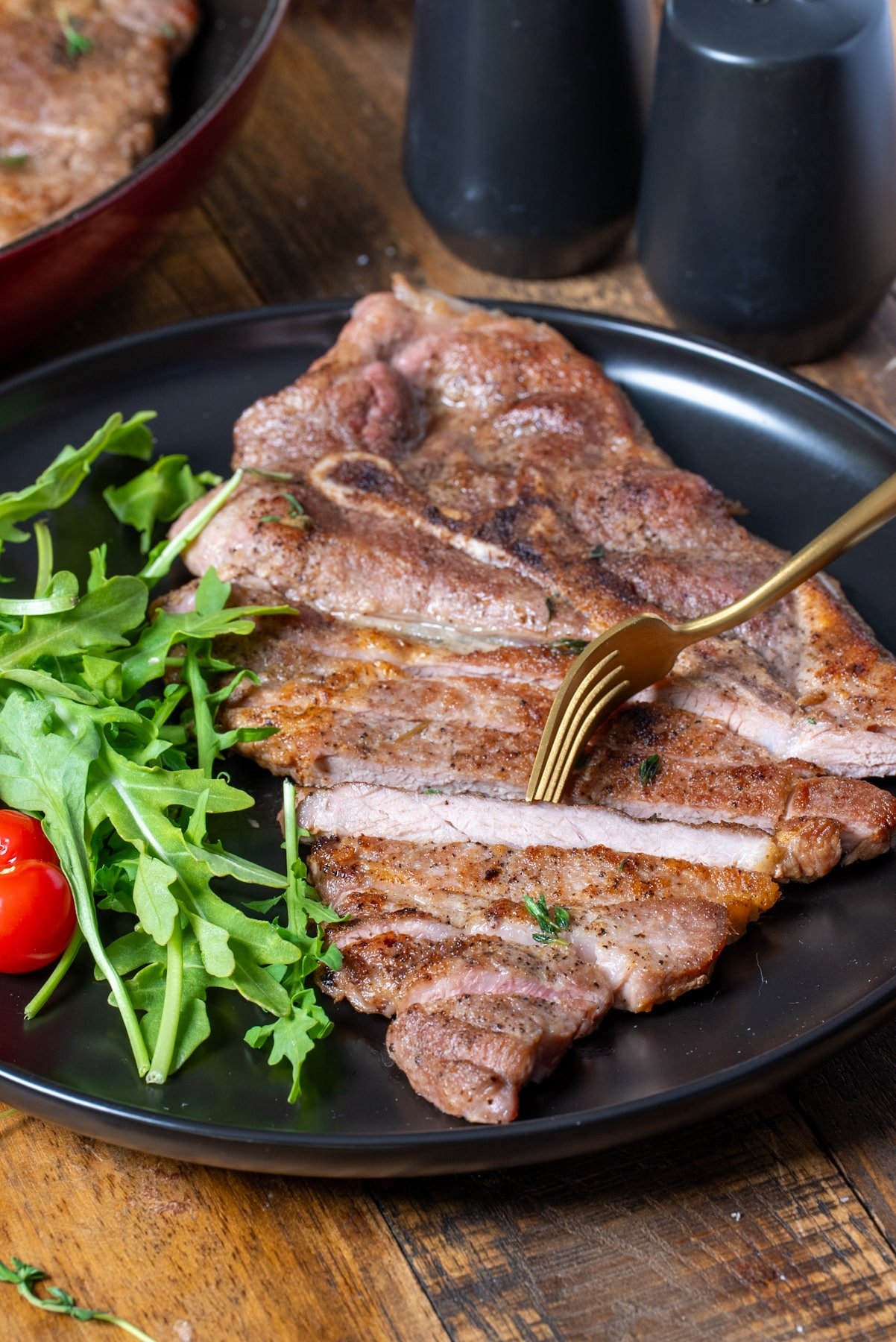cooked pork steak sliced on plate with salad with fork picking up steak