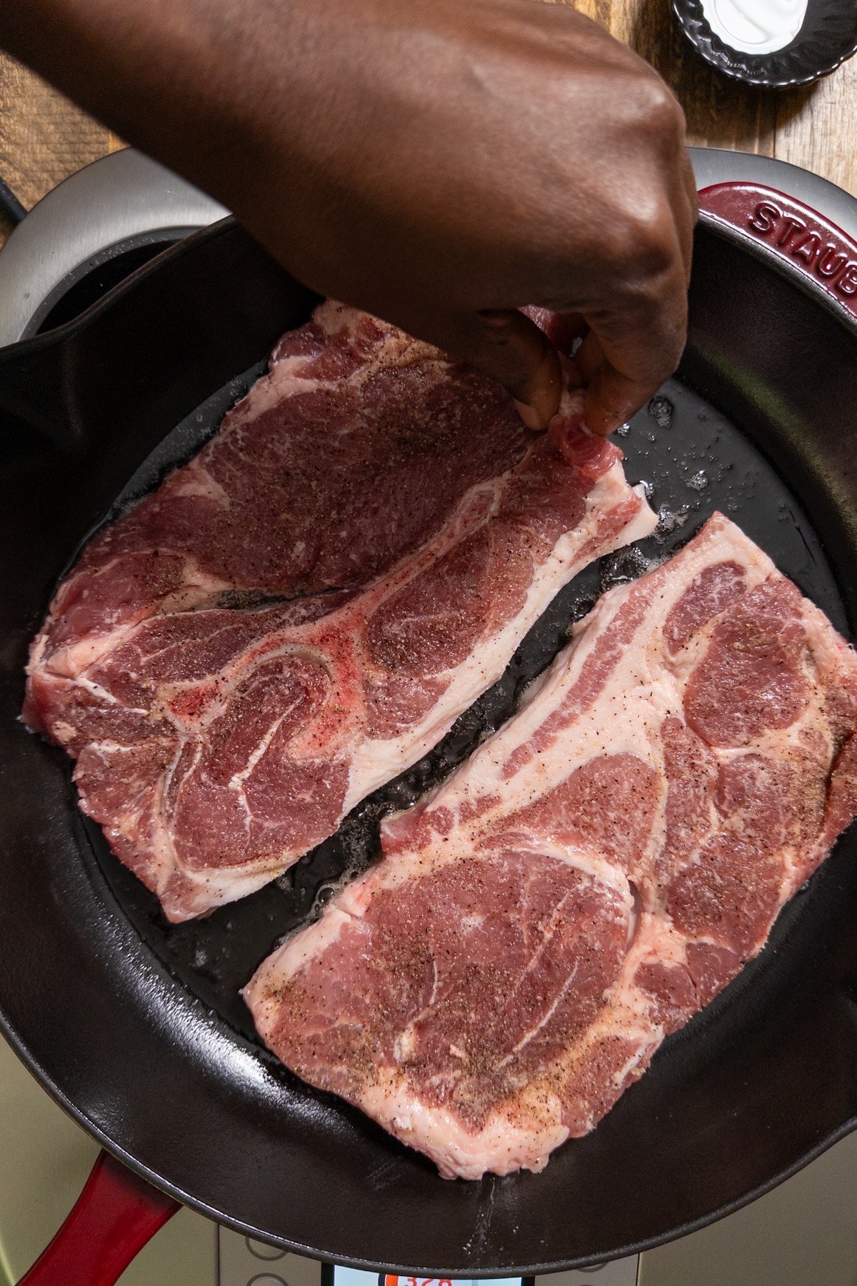 hand laying pork steaks in skillet