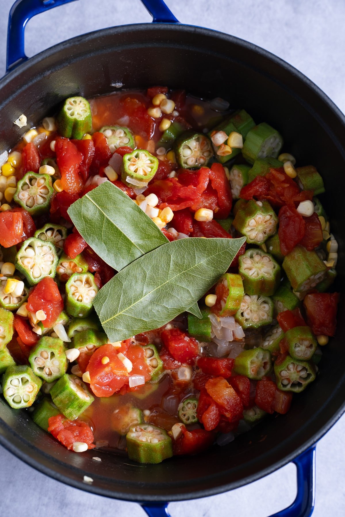 okra and tomato ingredients in pot with bay leaves on top