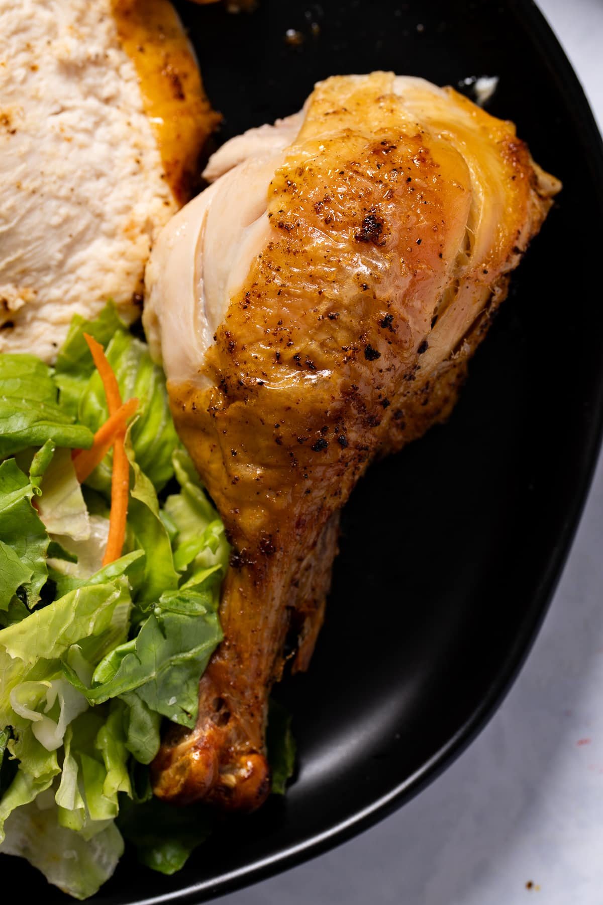 a chicken drumstick on a black plate with salad on the side