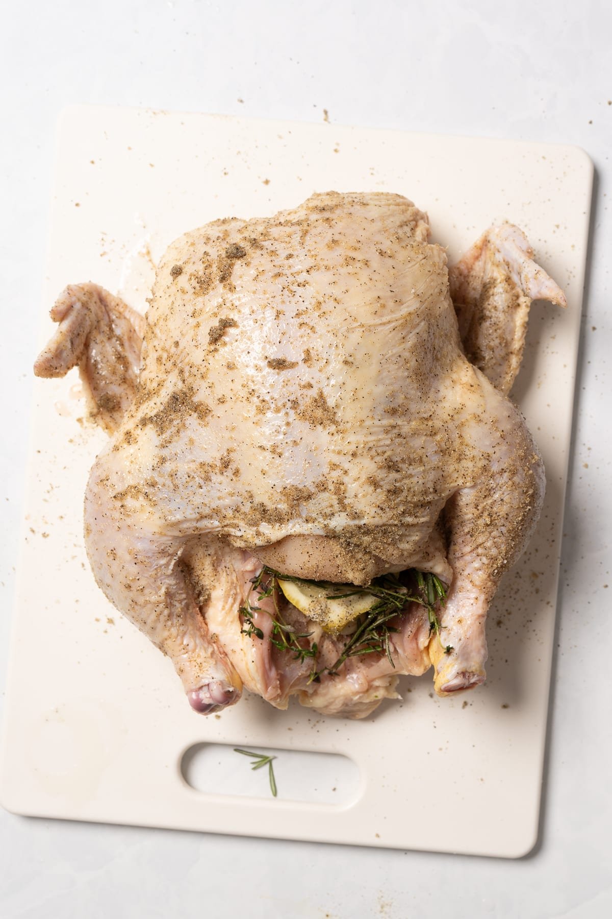 raw whole chicken on cutting board, seasoned