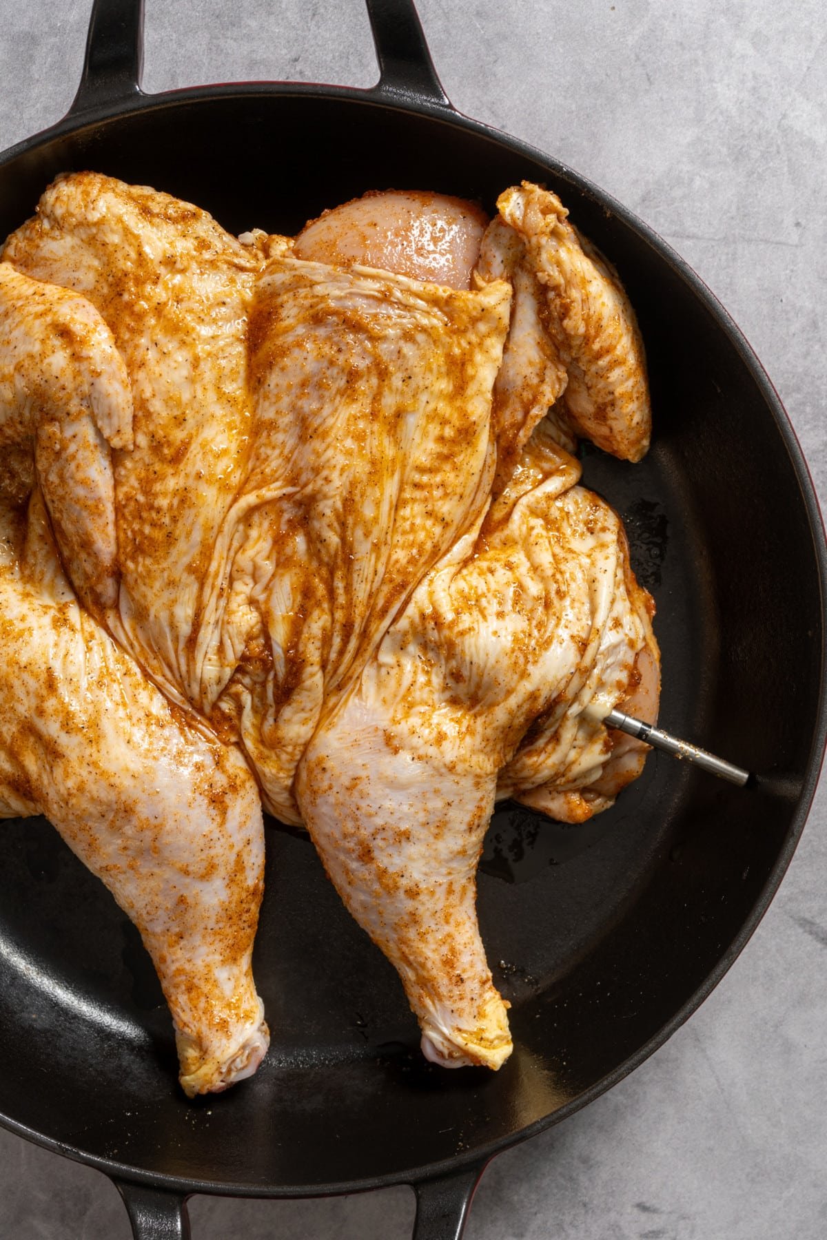 raw seasoned whole chicken in skillet with thermometer in thigh