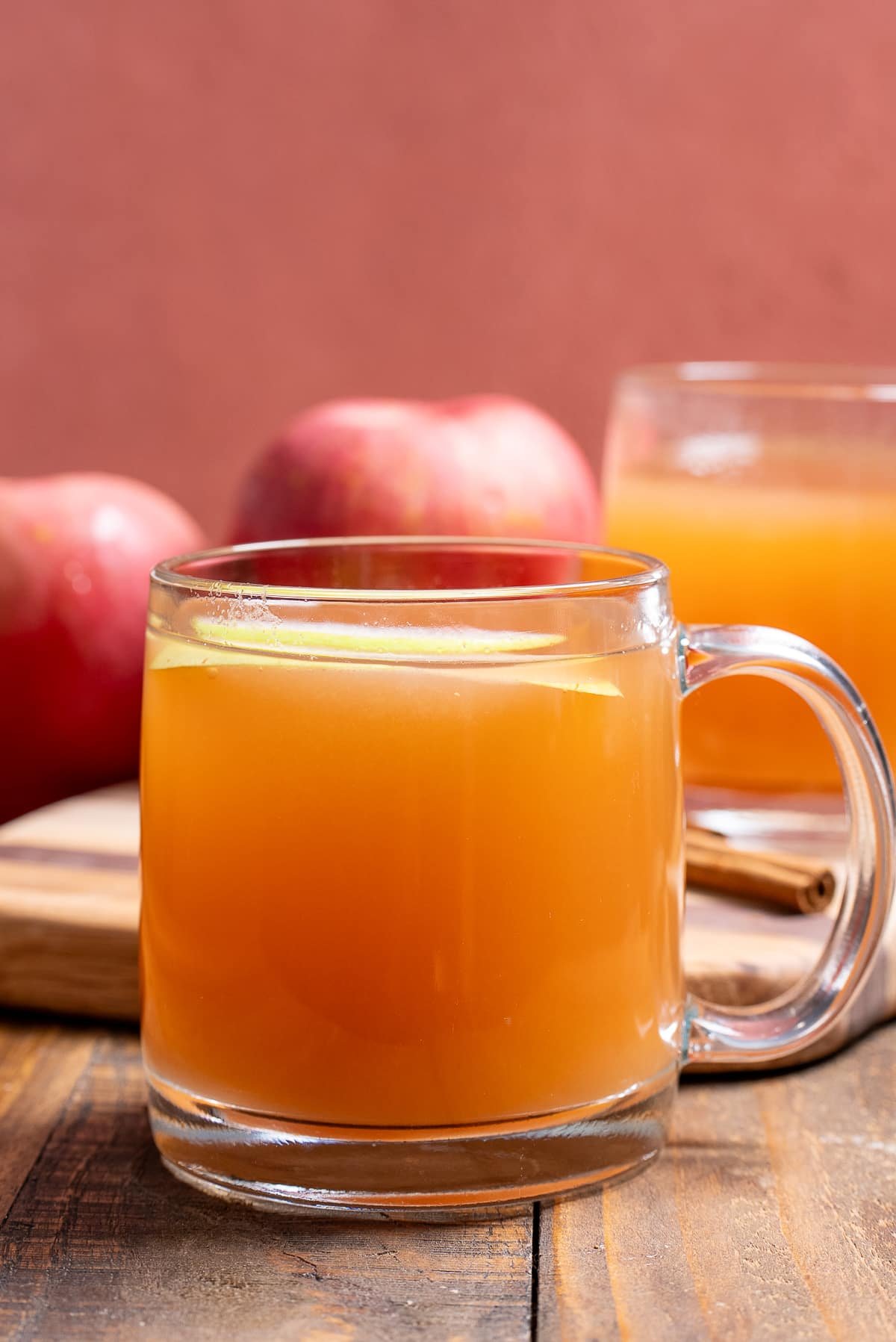 2 glasses of apple cider in mugs with apples in back