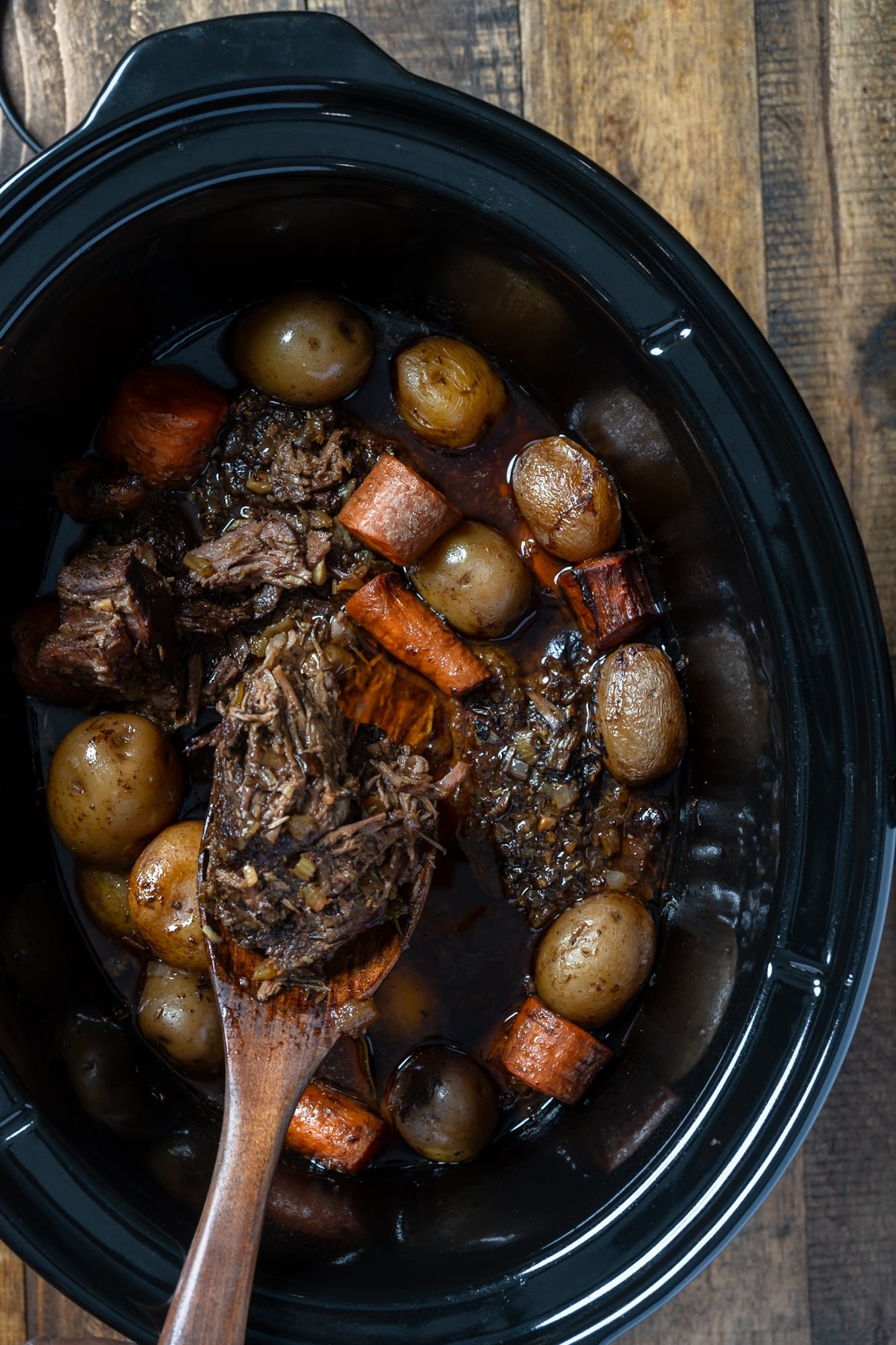 pot roast and vegetables after cooking for hours int he slow cooker with spoon picking it up
