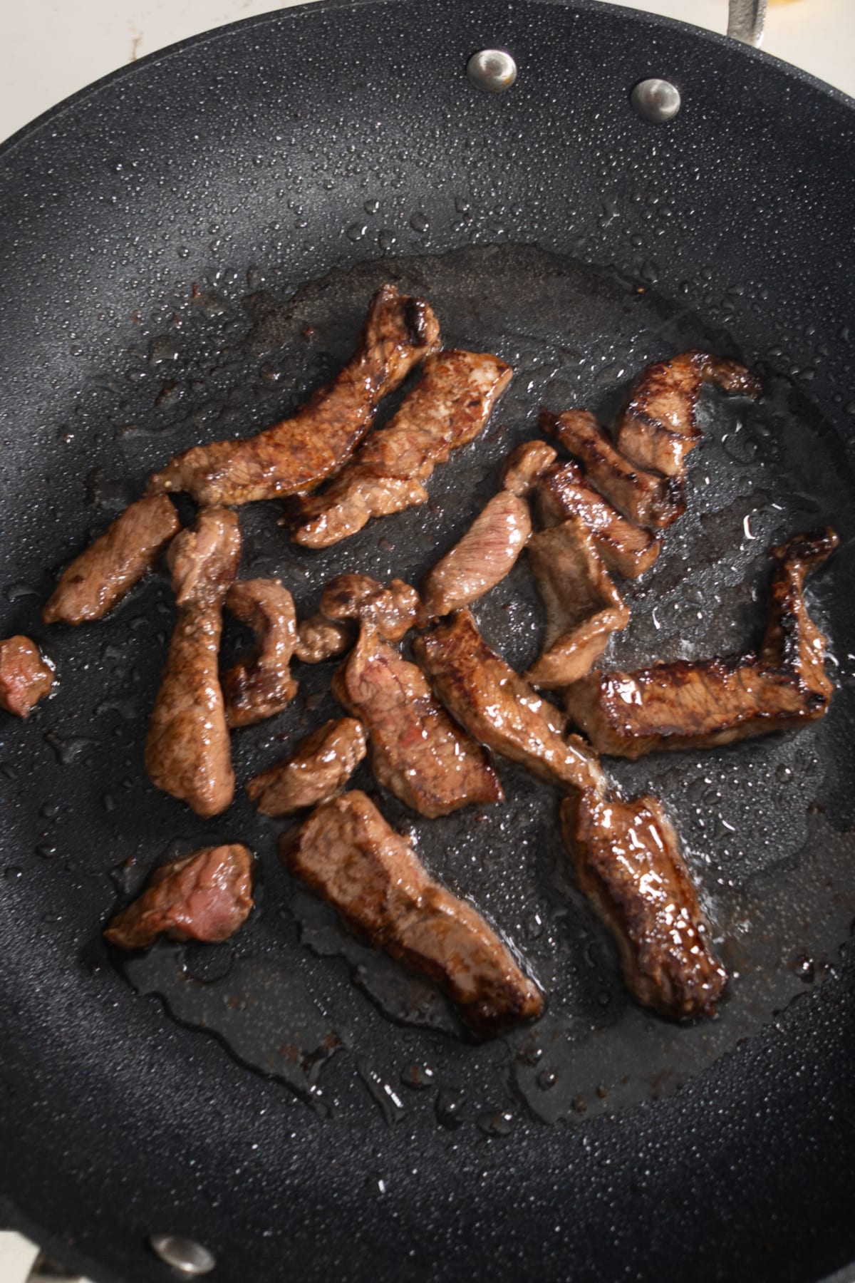 Steak pieces frying in a skillet.