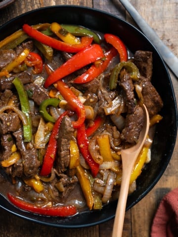 Jamaican pepper steak in a bowl with a spoon lifting up some of the pepper steak.