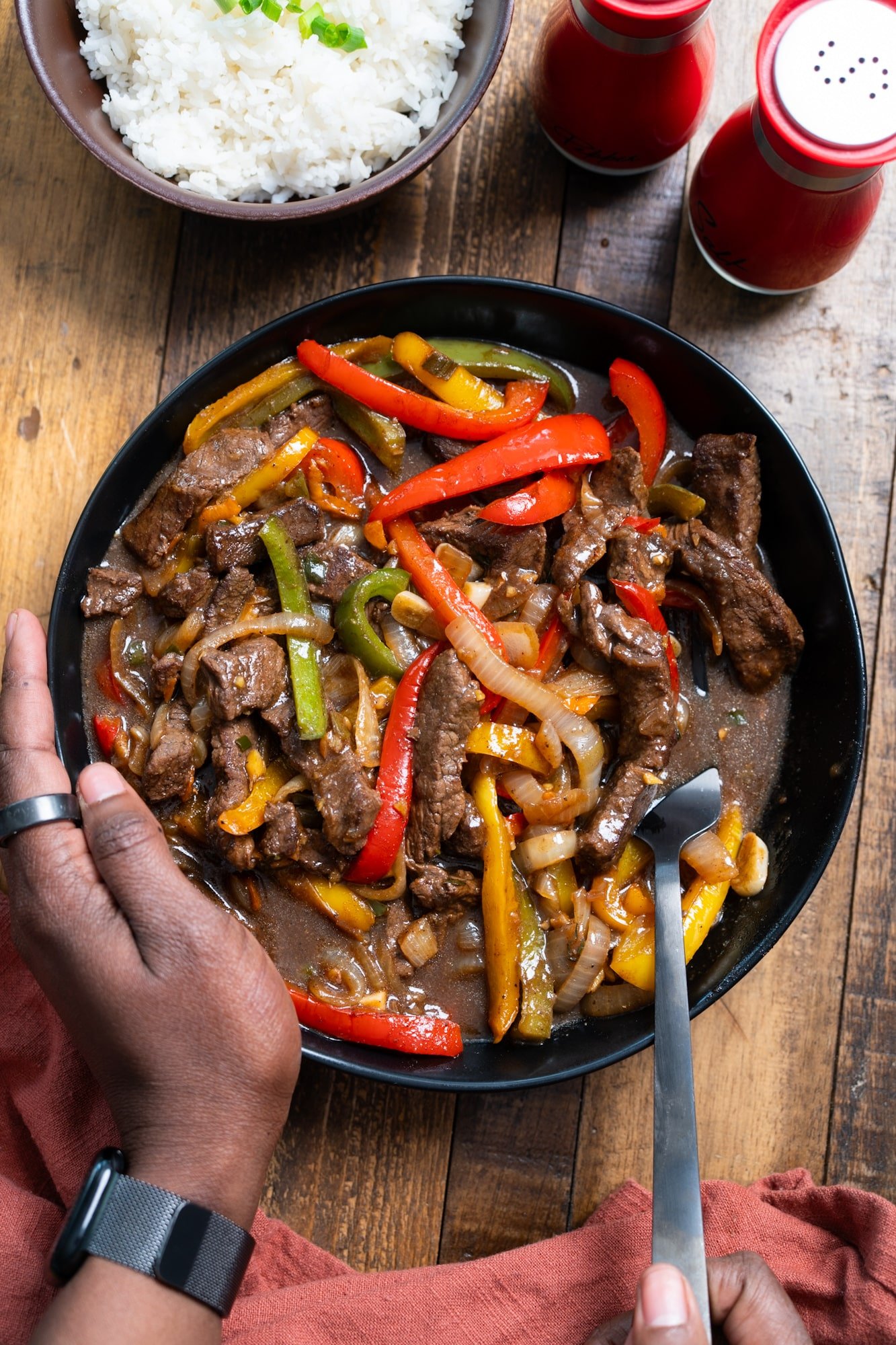 Hand holding bowl of pepper steak with fork picking up the steak.