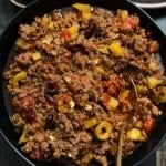Cuban picadillo and black bowl with gold spoon sticking out and olives on the side