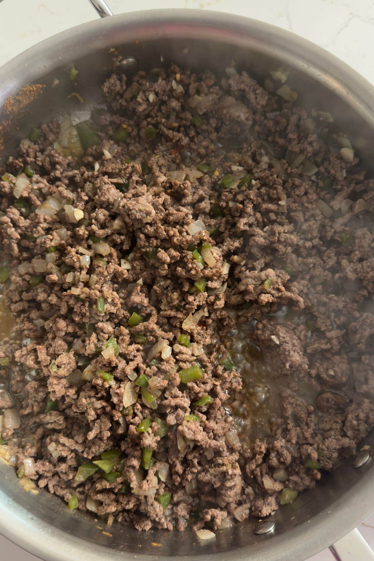 ground beef, yellow onion, and green bell peppers cooking in skillet
