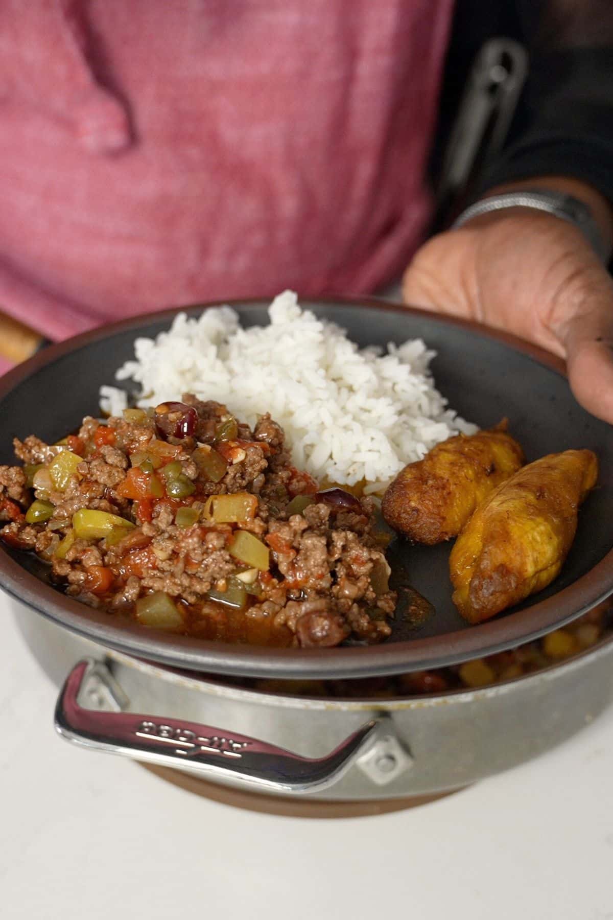 hand holding a plate with Picadillo, white rice, and plantains on the plate