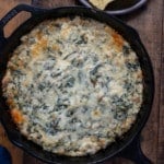 Spinach artichoke dip in skillet with tortilla chips on the side.