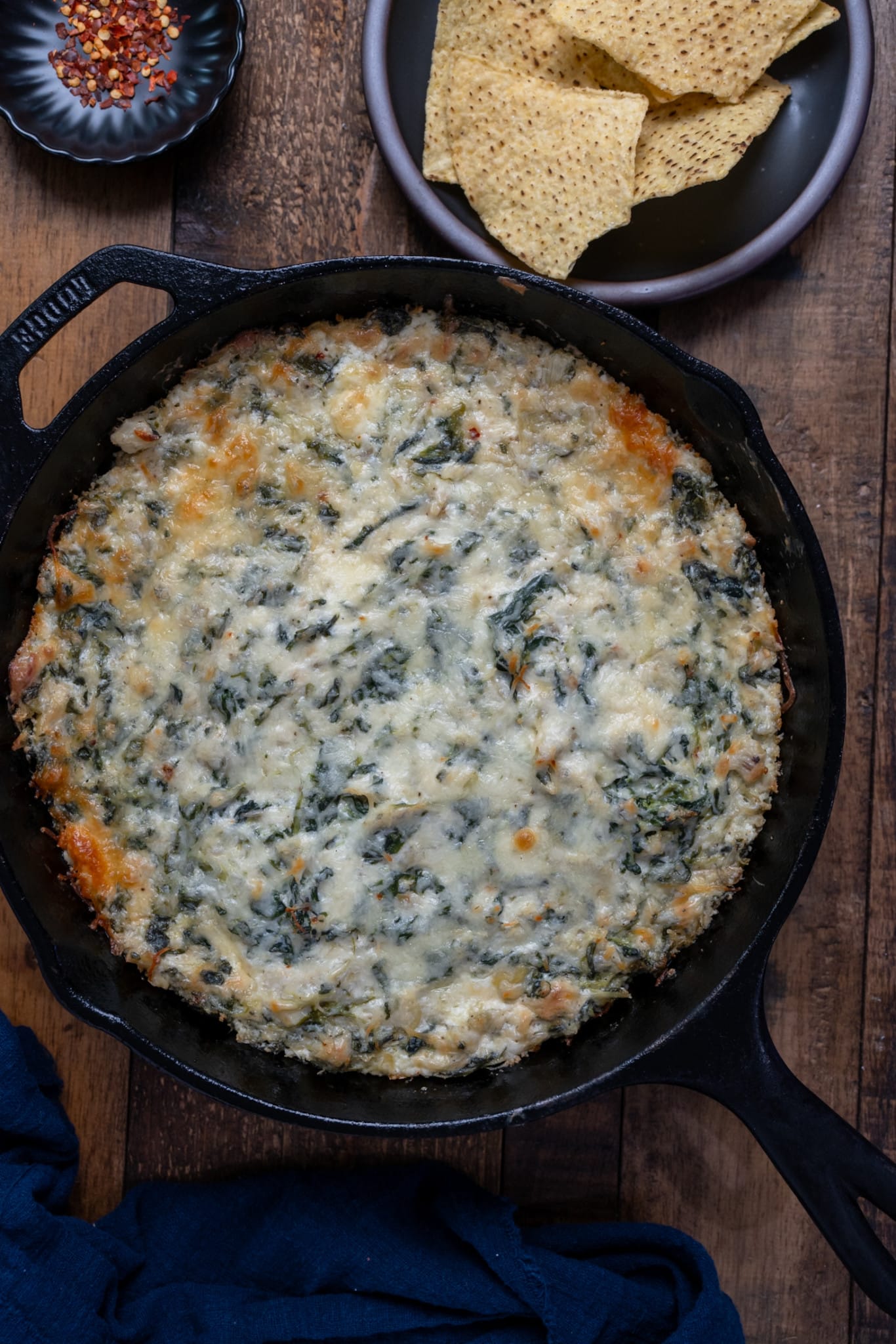 Spinach artichoke dip in skillet with tortilla chips on the side.