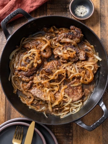 Liver and onions in skillet with salt and pepper on side