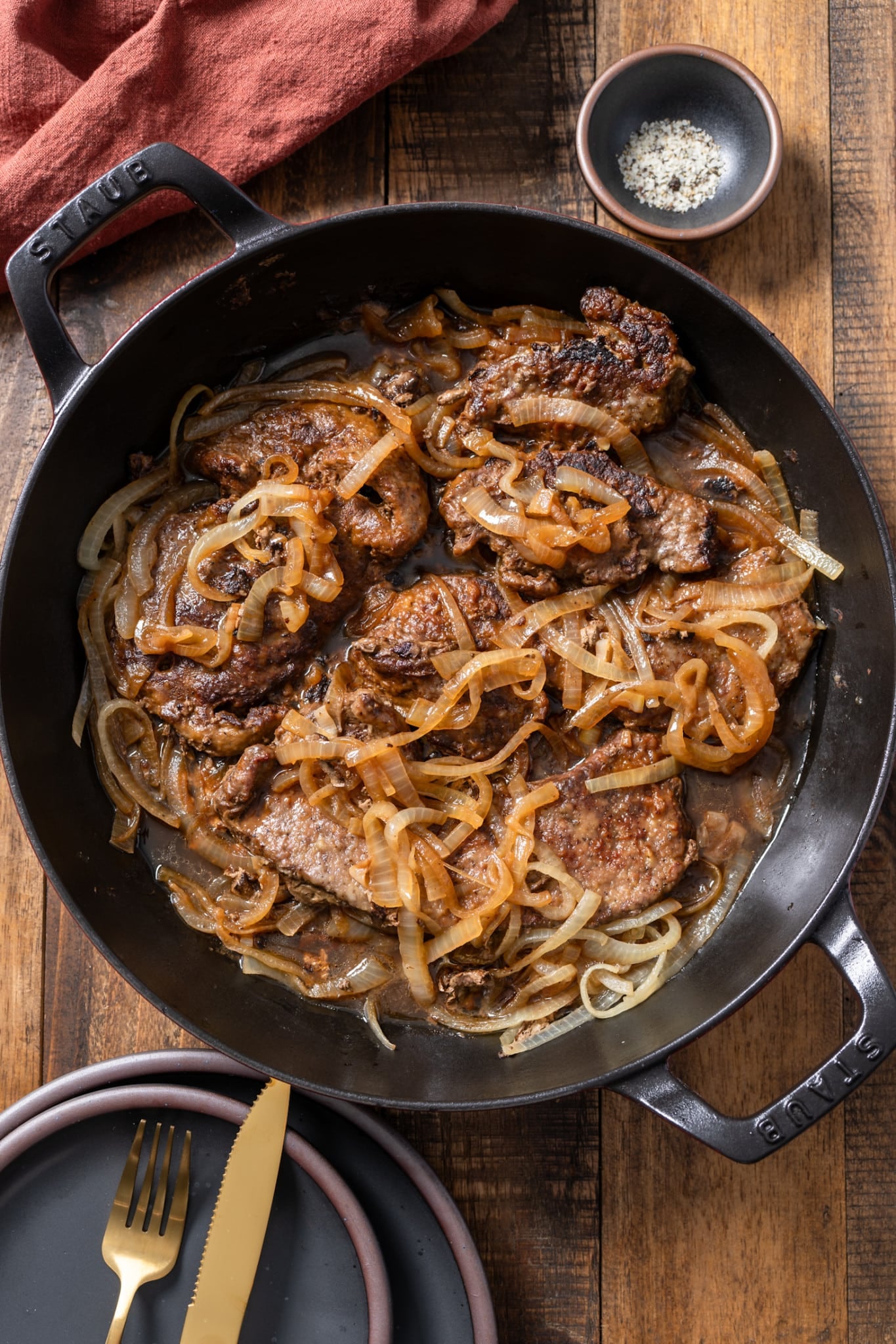 Liver and onions in skillet with salt and pepper on side