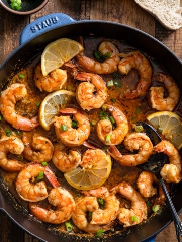 New Orleans-style BBQ shrimp in a skillet with a spoon and bread surrounding it