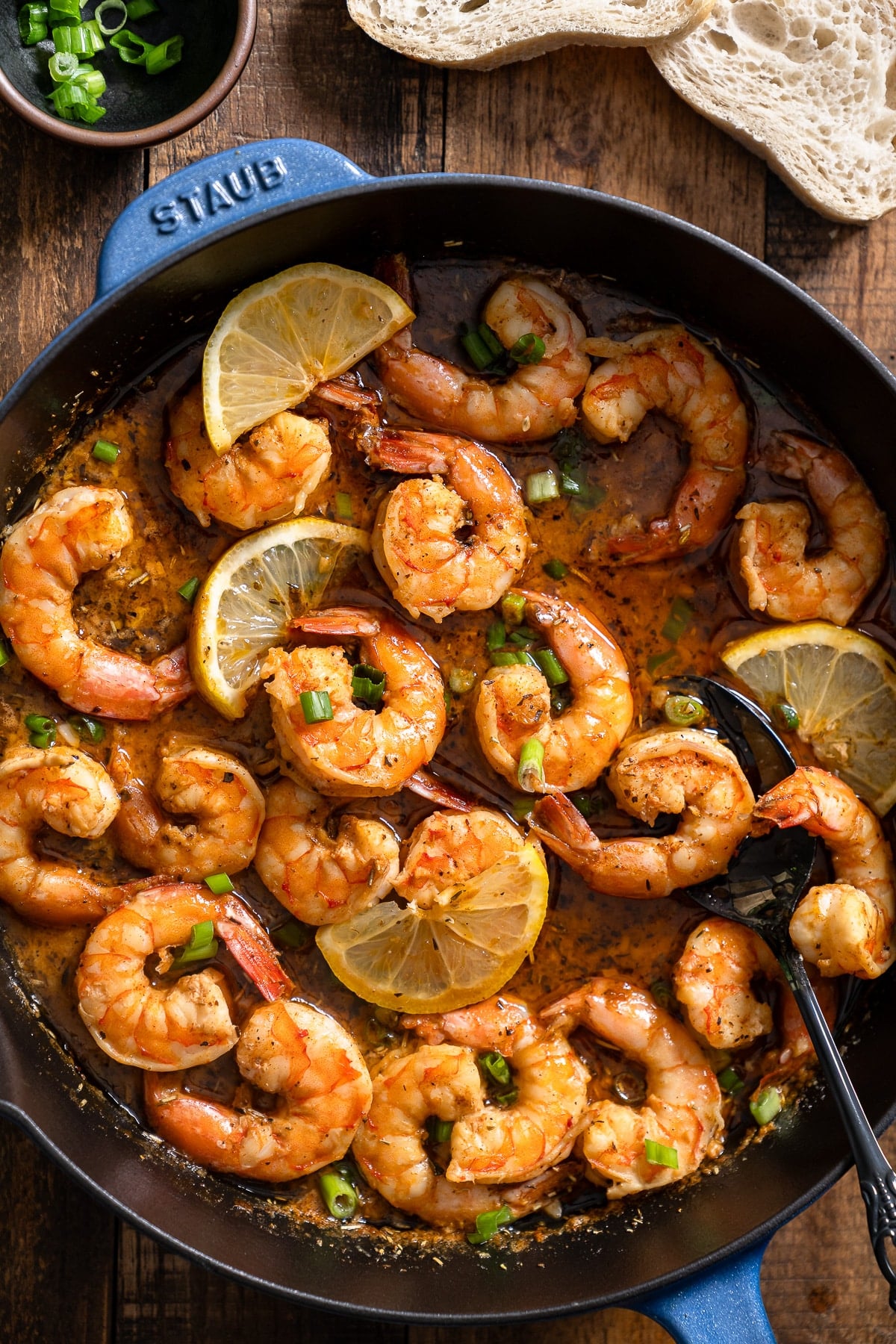 New Orleans-style BBQ shrimp in a skillet with a spoon and bread surrounding it