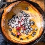 Dutch baby pancake in skillet with berries and powdered sugar on top