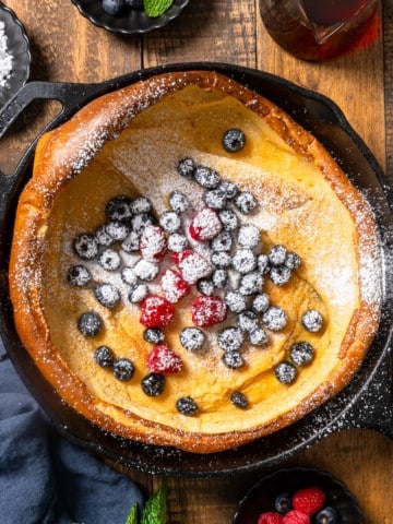Dutch baby pancake in skillet with berries and powdered sugar on top