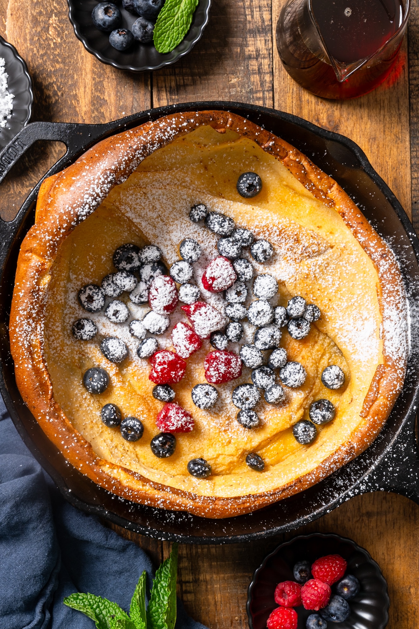 Dutch baby pancake in skillet with berries and powdered sugar on top
