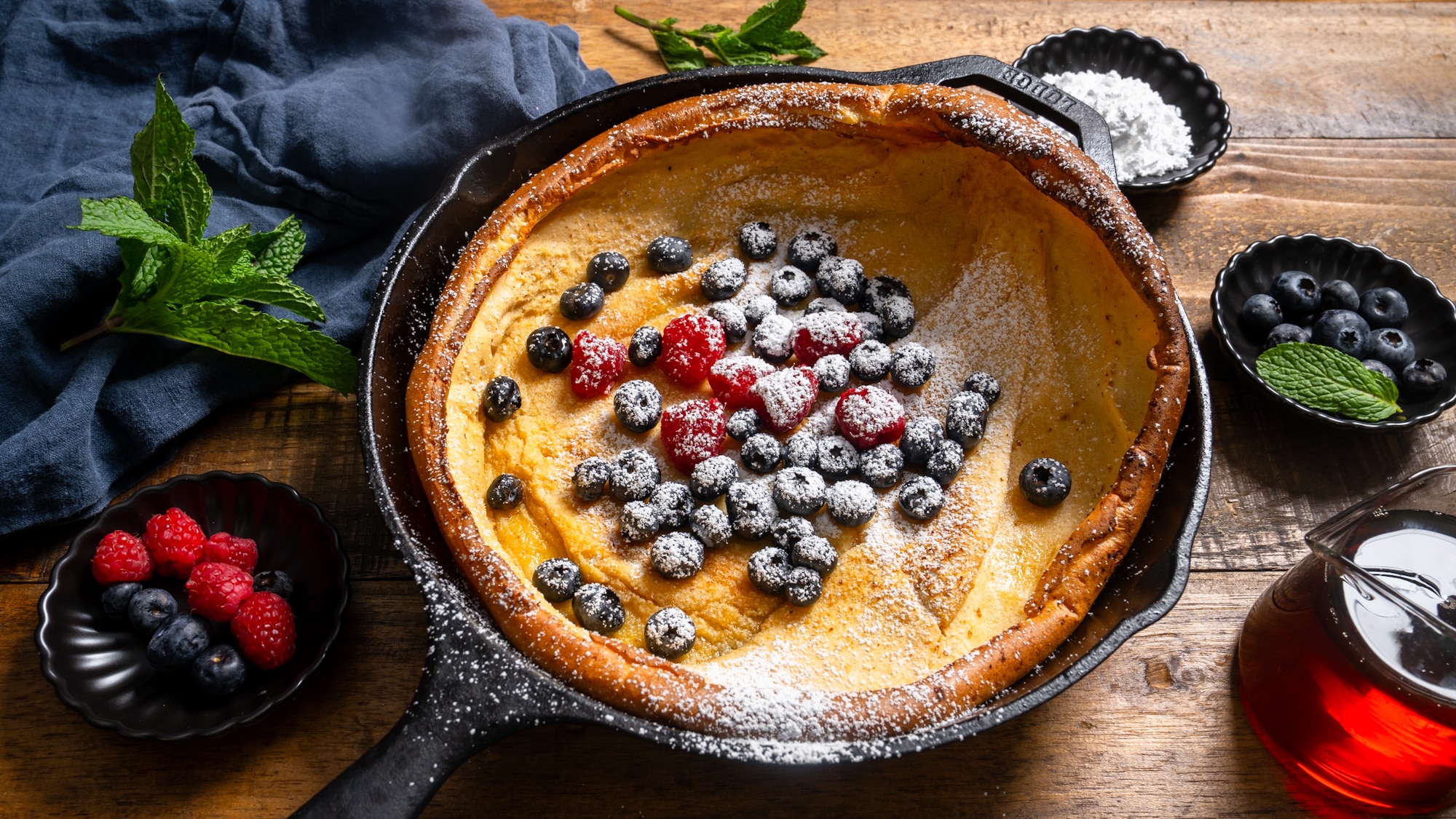 Dutch baby pancake in skillet with garnishes surrounding it
